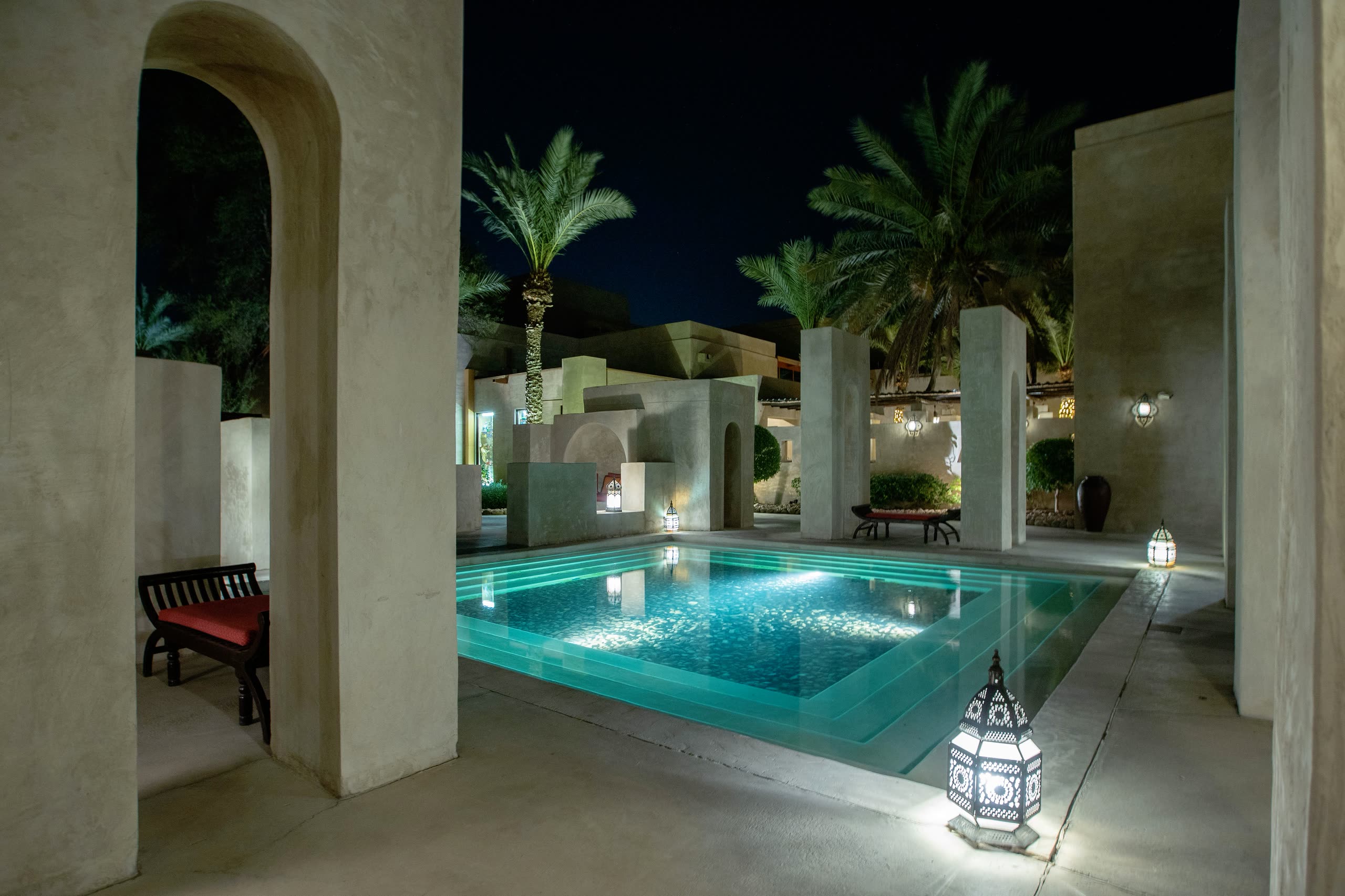 A lit courtyard pool at night, framed by stucco arches and lanterns